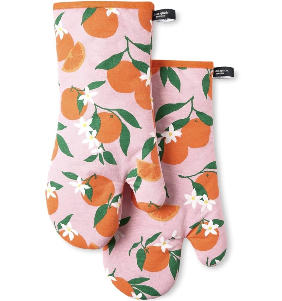 Two oven mitts with a vibrant pattern featuring oranges, green leaves, and white flowers on a pink background. Perfect for handling hot treats, they have black hanging loops with text labels, making them an ideal gift for Valentine's Day kitchen adventures.